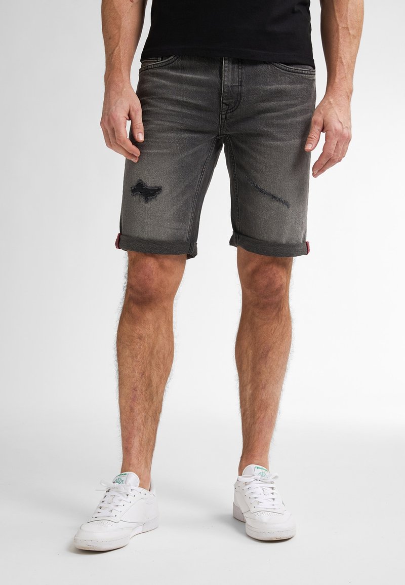 Grijze denim shorts met versleten details, opgerolde mouwen en een reguliere pasvorm. Gepaarde met witte sneakers, wat een casual look laat zien.