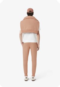 Rosa sweatshirt draperad över en vit t-shirt, matchad med passande tapered sweatpants och vita skor med bruna detaljer.