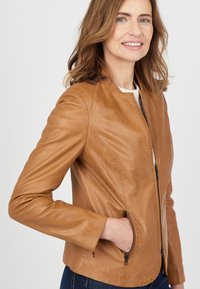 Bruine leren jas met een ronde kraag, slanke pasvorm en ritssluitingen. Glad materiaal met subtiele stikseldetails.