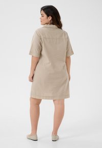 Abito a righe beige e crema con maniche corte e colletto, caratterizzato da una vestibilità morbida e un orlo diritto, realizzato in tessuto leggero.