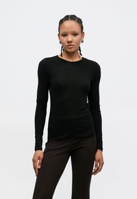 Haut noir à manches longues ajusté, en tissu lisse, avec un col rond et un design minimaliste. Associé à un pantalon marron ajusté.