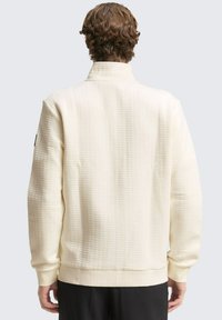 Crème-kleurige sweatshirt met een textuurstof, verhoogde patronen en geribde manchetten. Kenmerkt zich door een hoge kraag en een relaxte pasvorm.