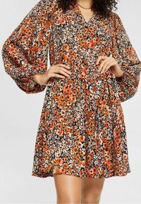 Blumenkleid mit Puffärmeln, V-Ausschnitt und taillierter Passform. Schwarzer Hintergrund mit orangefarbenen, weißen und rosa Blumenmustern.