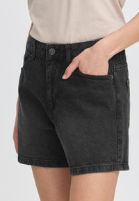Shorts en denim noir avec une coupe classique, featuring des poches latérales, passants de ceinture et une fermeture à bouton. Texture lisse et couture nette.