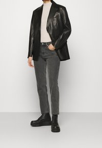 Blazer de cuero negro, suéter de cuello alto acanalado en gris claro, jeans grises y botas negras con cordones; look casual con materiales texturizados y diseño ajustado.