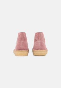 Botas de ante hasta el tobillo en rosa pálido con punteras redondeadas y suelas de goma beige. Diseño simple, sin herrajes ni patrones visibles.