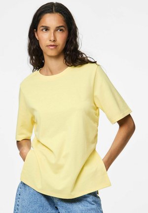 T-shirt jaune à manches courtes en coton léger, avec un col rond et une coupe décontractée. Associé à un short en denim bleu.