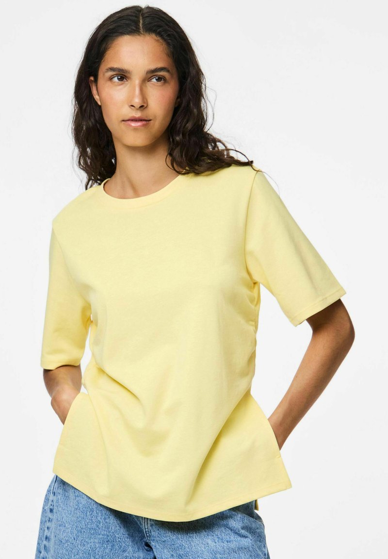 T-shirt giallo a maniche corte in cotone leggero, con scollatura rotonda e vestibilità rilassata. Abbinato a pantaloni corti in denim blu.