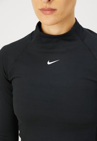 Schwarzes, langärmliges Sportoberteil mit hohem Kragen und weißem Nike-Logo auf der Brust. Hergestellt aus glattem, elastischem Material.