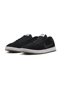 Crne nubuk tenisice s bijelim gumenim potplatima, s crnim Swoosh logom, teksturiranim gornjim dijelom i kontrastnim vezicama, na čistoj pozadini.