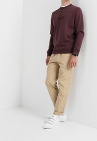 Felpa bordeaux con logo tonale, pantaloni beige e sneakers bianche. Fit casual con polsini a costine e scollatura a girocollo.