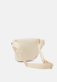 Beige tygmidjeväska med justerbar rem och plastspänne, visad mot en vit bakgrund.