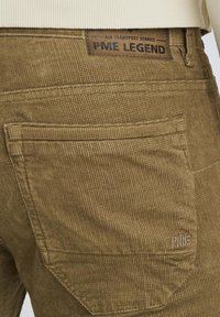 Pantaloni in corduroy marroni con cuciture e tasche visibili. Presentano una superficie texture e un'etichetta con la scritta "PME LEGEND." Design semplice.