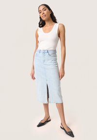 Gai zila džinsa svārki ar priekšējo spraugu, augstu jostasvietu un diskretām rotājumiem. Apvienoti ar baltu topiņu un melniem slingback apaviem.