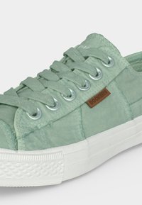 Baskets en tissu vert clair avec des lacets épais, des œillets métalliques, une semelle en caoutchouc blanche et une petite étiquette marron de la marque Dockers sur le côté.