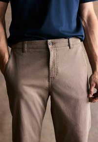 Beige kokvilnas chinos bikses ar pogu priekšpusē un slīpām kabatām, ar gludu tekstūru un taisnu kāju dizainu.