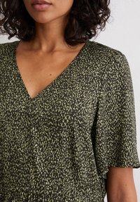 Short-sleeve dress in black with a green speckled pattern. Features a v-neckline and lightweight, textured fabric.