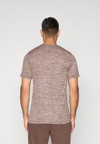 Camiseta de manga corta marrón con un patrón texturizado y jaspeado, cuello redondeado y corte relajado, vista desde la parte posterior.