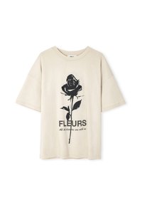 Béžové bavlněné tričko s krátkým rukávem. Obsahuje grafiku černé růže a text "FLEURS" spolu s "Všechny krásy jsou s námi" pod tím.