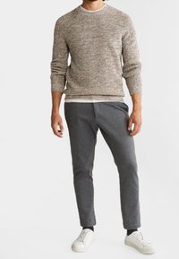 Grau strukturierter Pullover mit Rippung, kombiniert mit dunkelgrauen, schmal geschnittenen Hosen und weißen Sneakern. Einfaches Design, lässiger Stil.