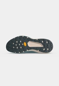 Semelle de chaussure vert foncé et beige avec un motif hexagonal et un petit logo jaune au centre sur un fond clair uni.