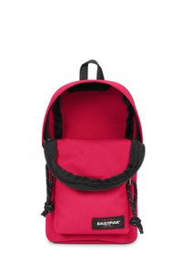 Röd tyg ryggsäck med svart dragkedjestängning och justerbar rem. Har en liten framficka och handtag på toppen för enkel bärning.