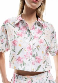 Blomstrede kortærmede skjorte i hvid med pink og grønne blomstermønstre, knaplukning og et cropped design. Blød stoftekstur.
