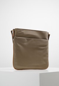 Khaki nylon crossover taske med en glat overflade, rektangulær form, enkelt rem og en forlommer omkranset af brune læderdetaljer.