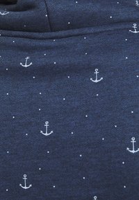 Tissu bleu foncé avec de petites ancres blanches et des points imprimés dans un motif dispersé.