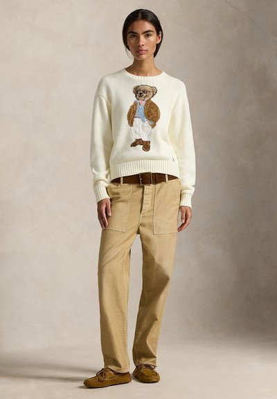 Εκρού πλεκτό πουλόβερ με σχέδιο αρκούδας σε καφέ και μπλε, συνδυασμένο με ταμπά παντελόνι cargo και καφέ μοκασίνια.