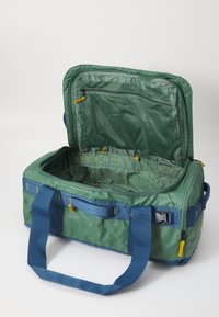 Green and blue fabric duffel bag with yellow accents, features a large zippered opening, mesh pocket, and sturdy carrying handles.