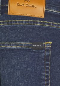 Mörkblå denimjeans med gul sömnad, försedda med läder- och tygmärken präglade med "PS Paul Smith."