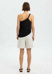 Svart top med en axel och flätad rem, tillsammans med ljusgrå shorts. Toppen har en slät yta och asymmetrisk design.