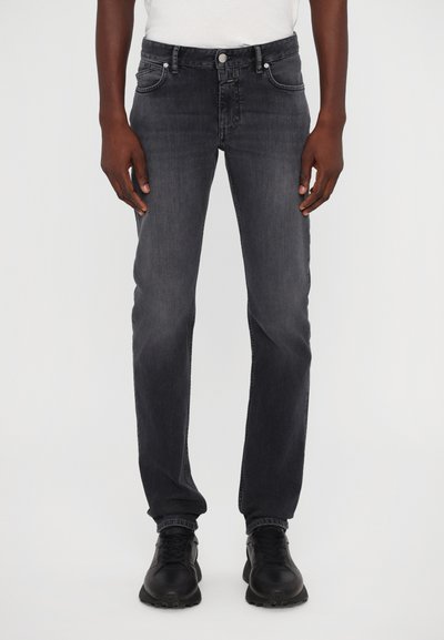 Dunkelgraue Denim-Jeans mit geradem Schnitt, Fronttaschen und Knopfverschluss. Kombiniert mit schwarzen Sneakers für einen Kontrast.
