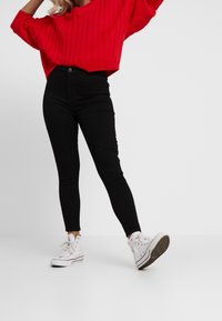 Suéter de punto acanalado rojo con silueta holgada, combinado con jeans skinnies negros. Zapatillas altas blancas completan el atuendo.