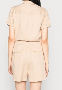 Servizio corto beige con maniche a sbuffo, colletto, maniche arrotolate e tasche posteriori. Realizzato in tessuto leggero con una texture liscia.