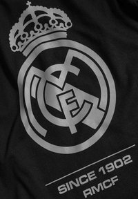 Svart tyg med en stor silver Real Madrid-logotyp och krona, med texten "SINCE 1902 RMFC" under emblemet.