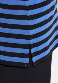 Randig topp med breda svarta och ljusblå ränder, korta ärmar och en sidoklyfta vid fållen. Tillverkad av mjukt, lätt material.