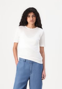 Weißes T-Shirt mit kurzen Ärmeln aus leichtem, transparentem Stoff und Rundhalsausschnitt, kombiniert mit hellblauen weit geschnittenen Hosen.