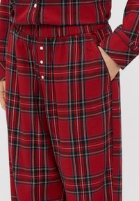 Rot kariertes Pyjama-Set aus einem gebürsteten Stoff. Mit Knöpfen auf der Vorderseite des Shirts und einem elastischen Bund mit Taschen in der Hose.