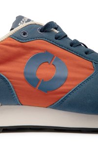 Gros plan sur le côté d'une basket bleue et orange avec un symbole circulaire de recyclage et des lacets bleu marine sur fond blanc.