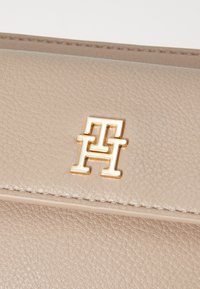 Sac en cuir texturé beige avec un logo entrelacé en métal doré à l'avant, rehaussé de coutures le long des bords.