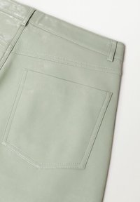 Pantalones de piel color verde menta con un bolsillo trasero, textura suave y detalles de costura sutiles. Primer plano del diseño del bolsillo.
