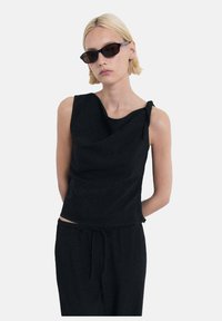 Top nero senza maniche con design drappeggiato e dettaglio a nodo sulla spalla, abbinato a pantaloni neri con coulisse. Tessuto dalla superficie liscia.