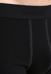 Zwarte katoenen boxershorts met een gladde textuur, voorzien van een effen zwarte tailleband met de opdruk "SLOGGI" en contrasterende grijze stiksels.