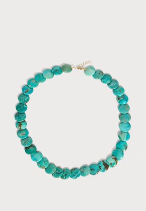 Turkoois stenen ketting met ronde platte kralen en een gouden ketting sluiting op een effen lichte achtergrond.