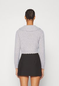 Ljust grå, stickad, kort hoodie med en texturerad, dekorerad krage och vågig nederdel, kombinerad med en svart kjol.