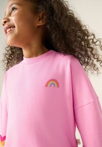 Rosa Langarm-Sweatshirt aus weichem Stoff, mit einem gestickten Regenbogenmuster auf der Brust und einem gerippten Kragen.