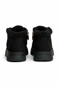 Botines de ante negros con un suave forro de piel sintética negra, cierre de cremallera y una suela de goma negra texturizada con un ligero tacón.