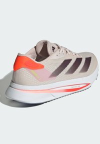 Světle béžová běžecká bota Adidas s tmavými pruhy, jasně oranžovým podpatkem a bílou podrážkou s nápisy "Lightstrike Pro" a "Adizero SL 2".